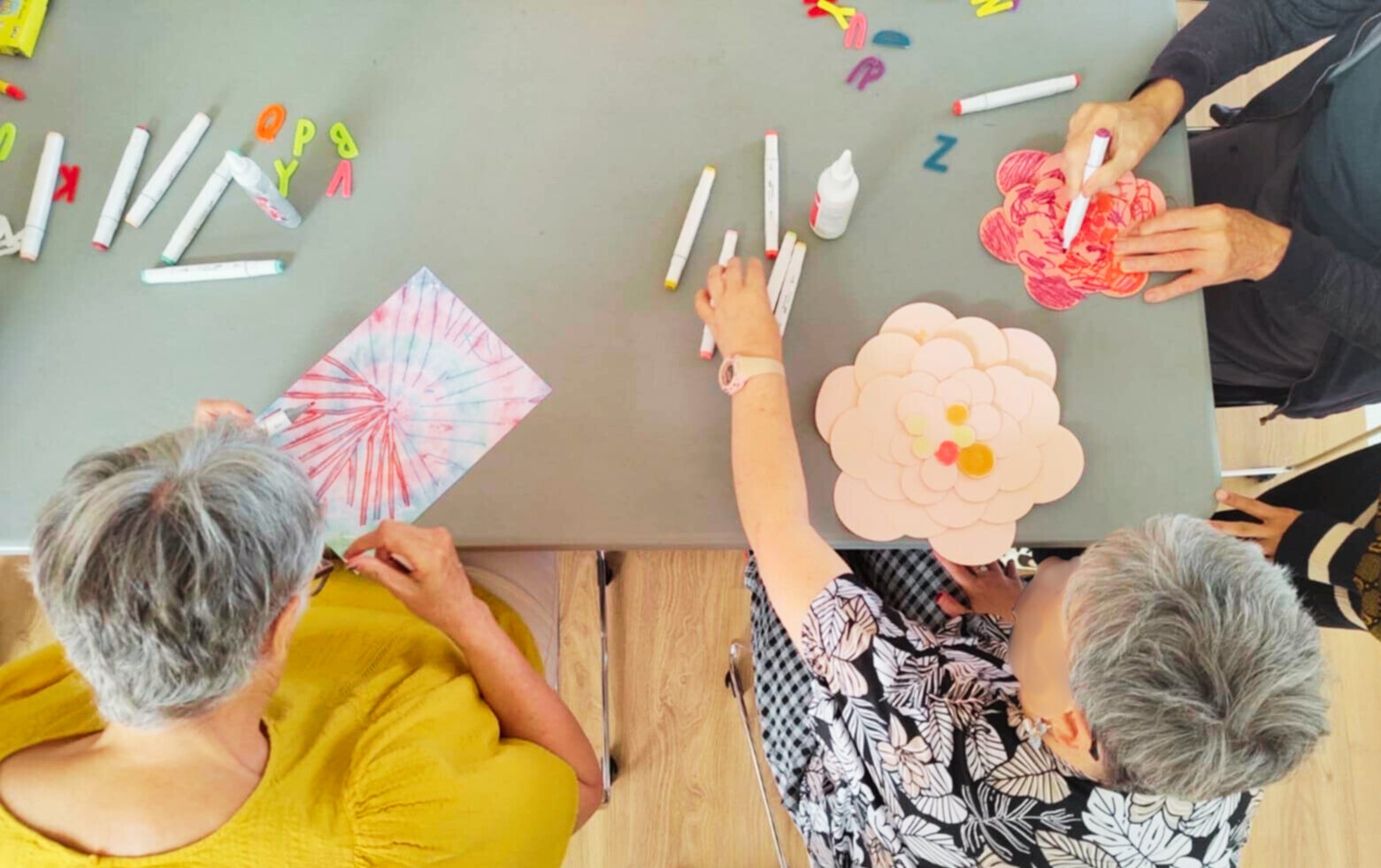 A birds eye view of two participants doing a therapeutic arts activity using coloured paper and felt tip pens.