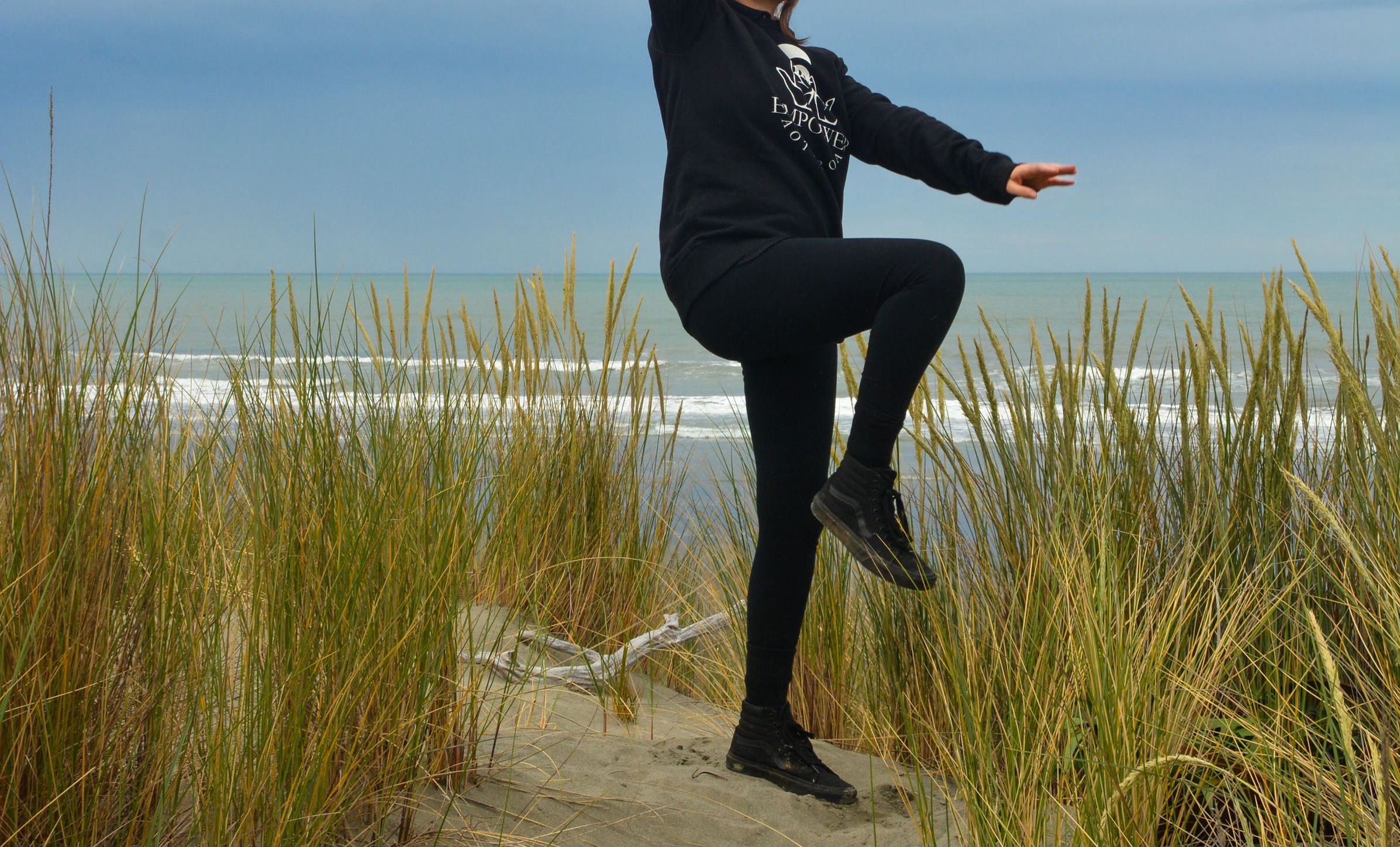 Someone dancing in black clothes on a beach, cropped shoulders down.